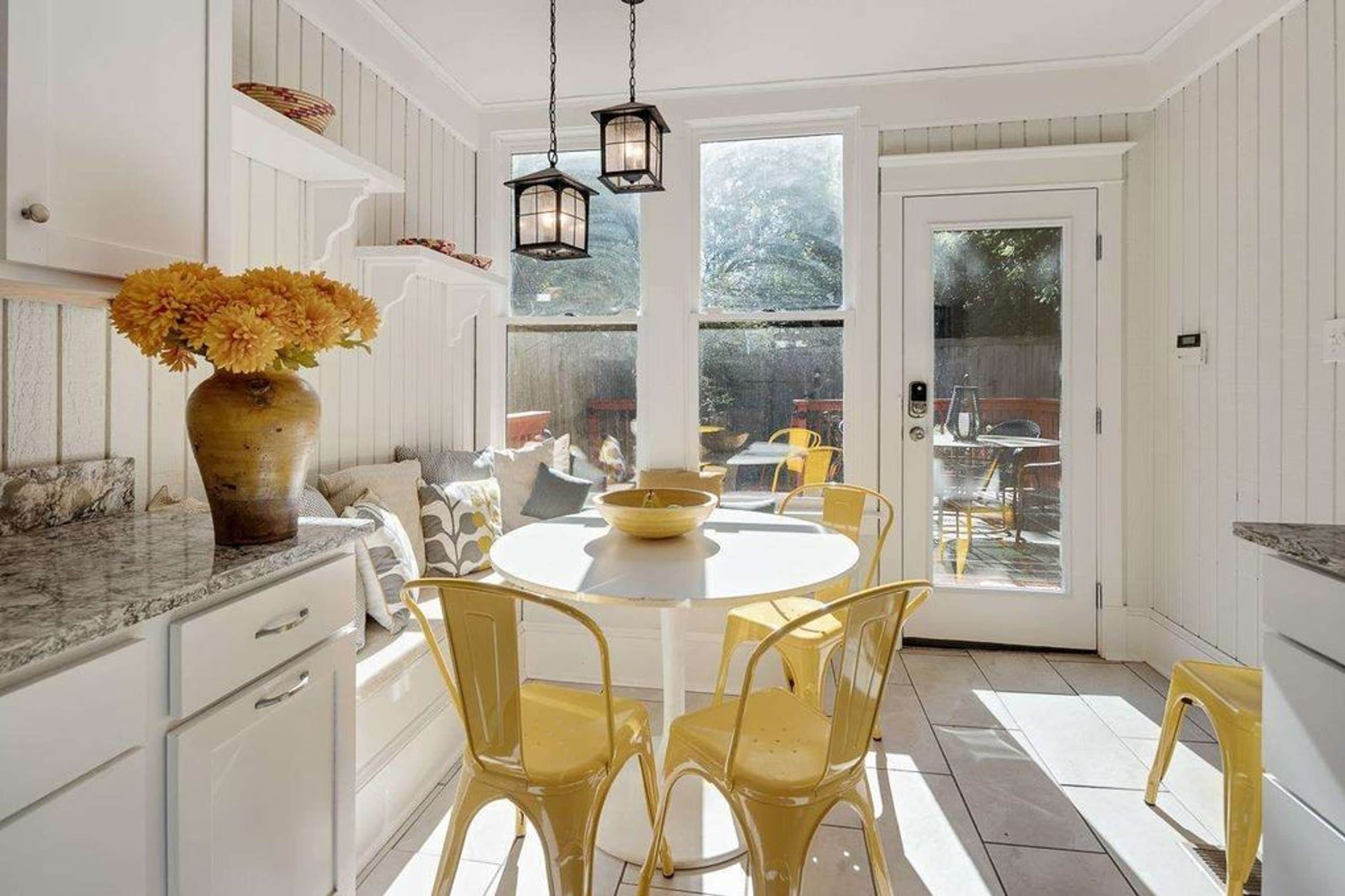 A kitchen with white cabinetry, a round dining table, yellow chairs, and a vase with flowers.