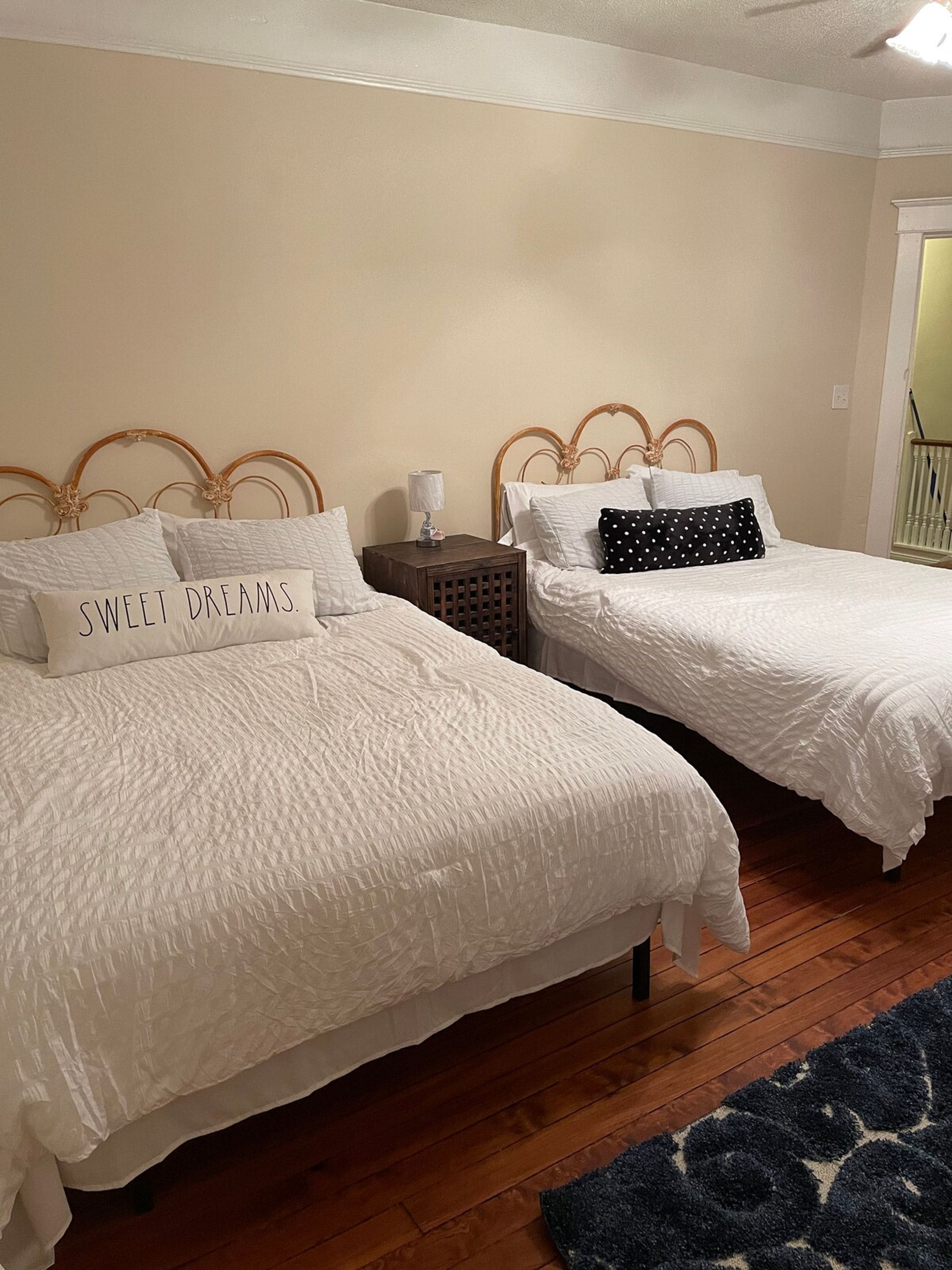 Two single beds with headboards, a bedside table with a lamp, and a dark blue rug on a wooden floor.