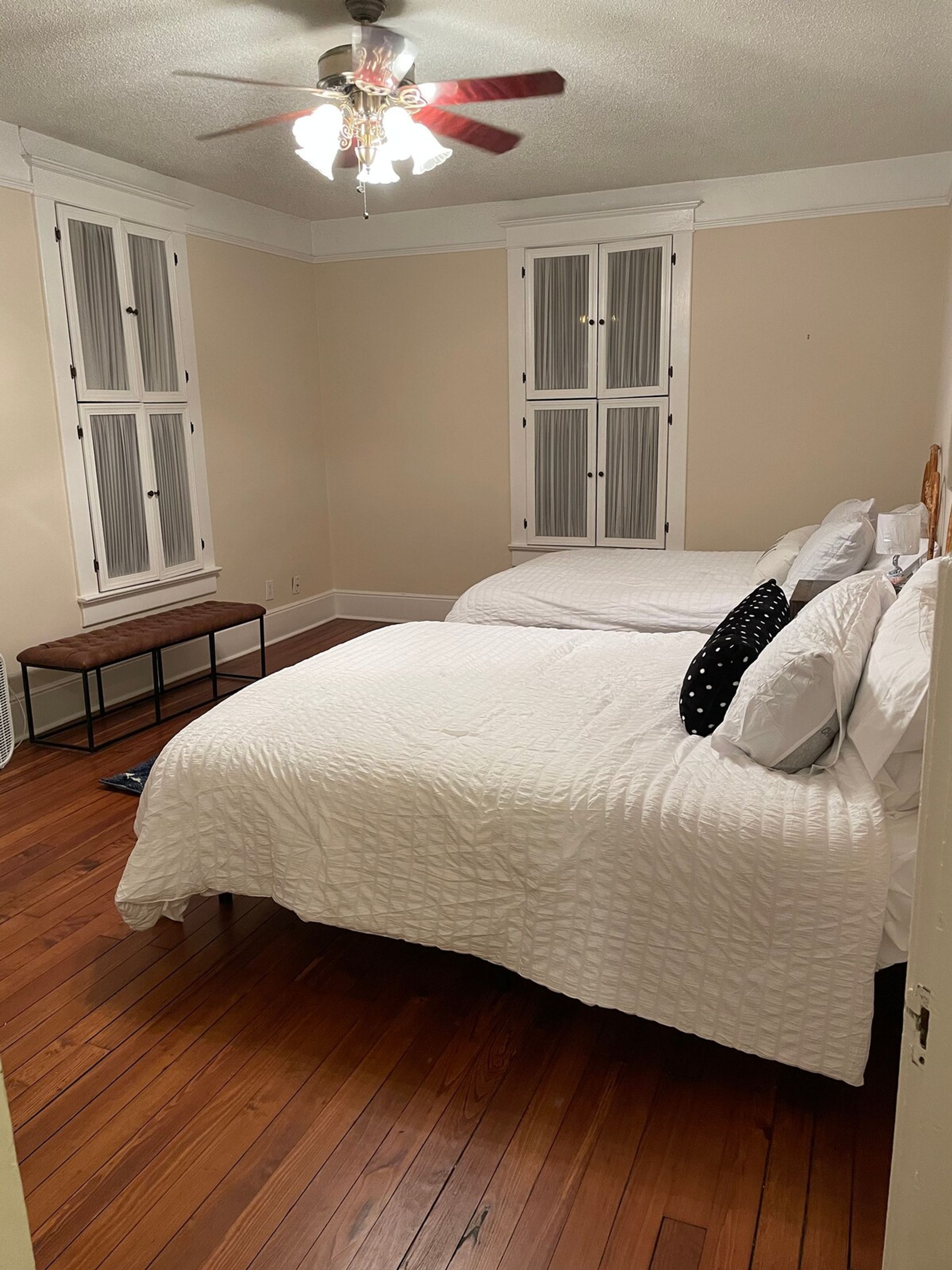 A bedroom with a queen-sized bed, a ceiling fan, and two windows with curtains.