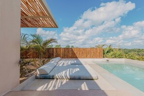 Ein Poolbereich mit Holzterrasse, Liegestühlen und Blick auf Himmel und Vegetation.