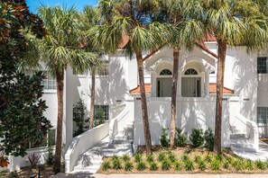 A white building with a red-tiled roof, a central staircase, and palm trees. - Golf Course View Villa With Luxury 6 Seater Golf Cart Steps to Beach Pool Tram Just Across From Entry (Miramar Beach)