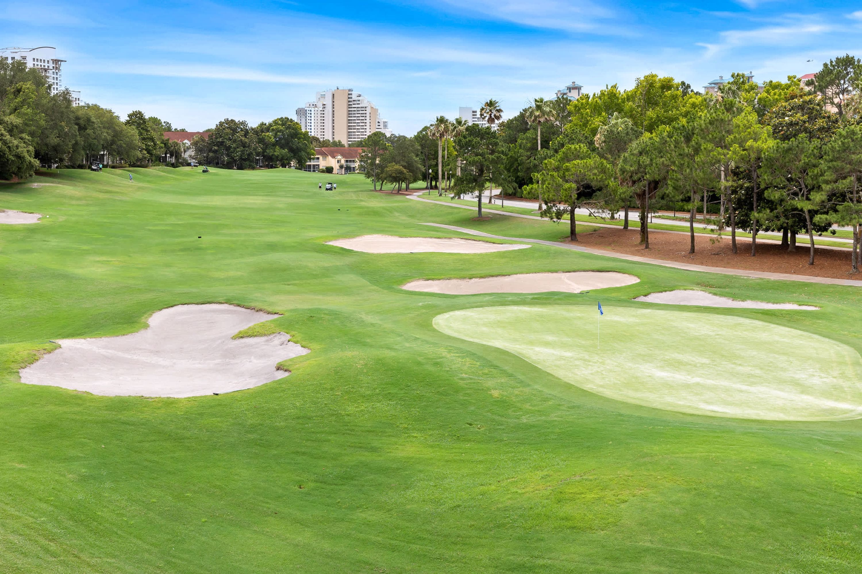 A golf course with sand bunkers, trees, and a clear sky.