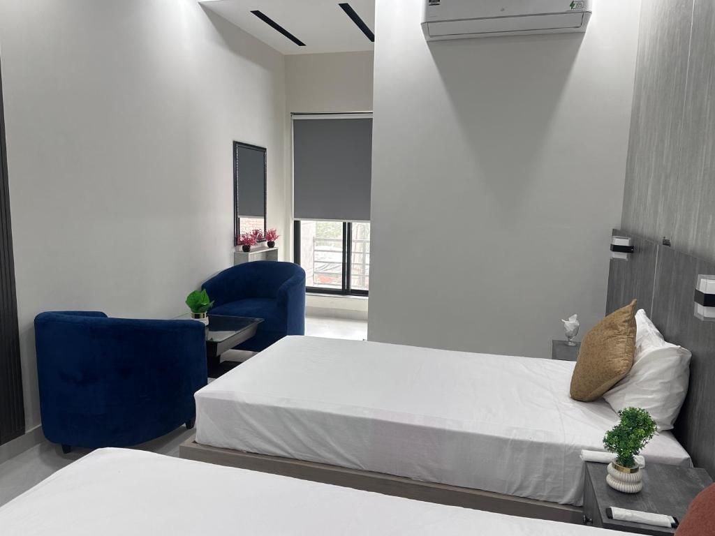 Una habitación de hotel moderna con una cama, un sillón azul, una mesita y una planta en maceta.