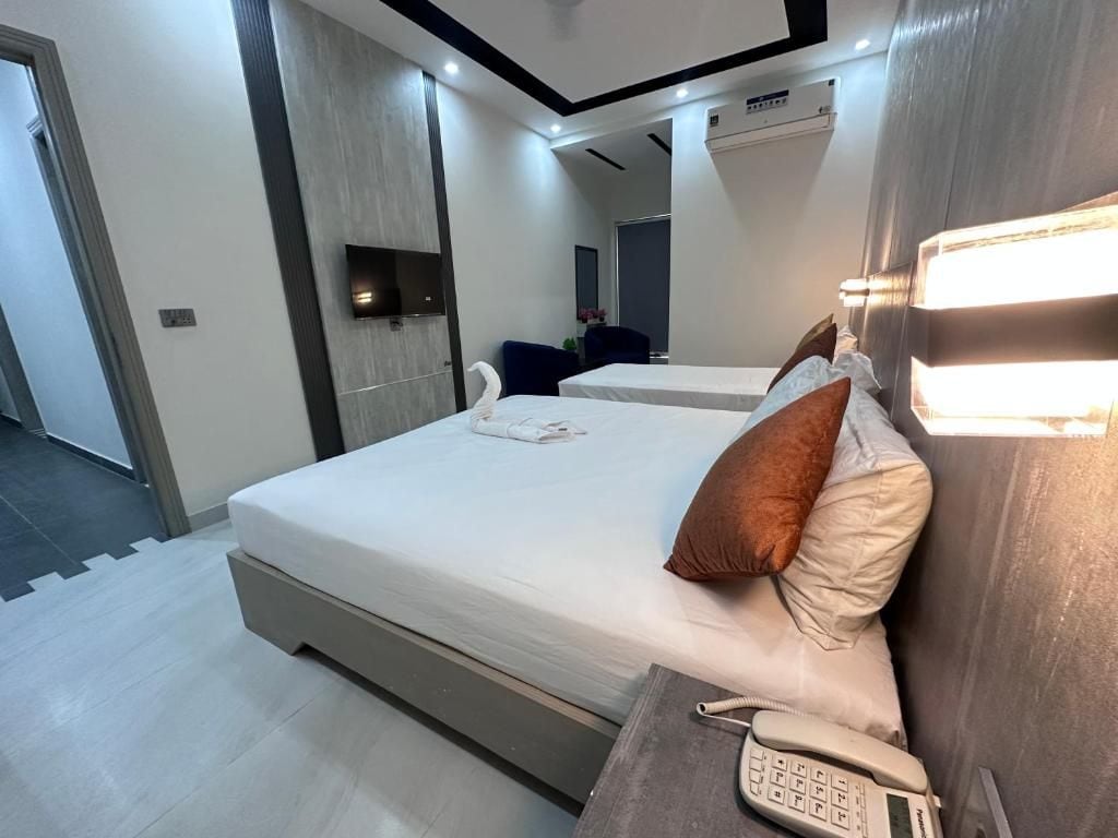 A modern hotel room with a large bed, a bedside telephone, and a wall-mounted TV.