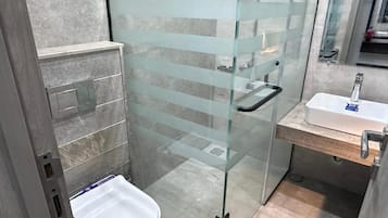 A modern bathroom with a glass shower enclosure, a white sink, and a wooden vanity.