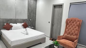 A modern bedroom with a bed, a glass coffee table, a tufted armchair, and a wardrobe.