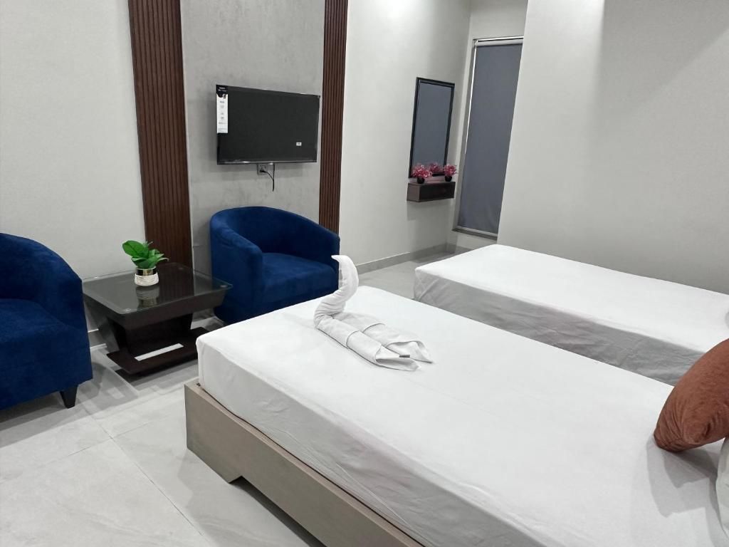 A hotel room with two beds, a flat-screen TV, a small table with a plant, and blue armchairs.