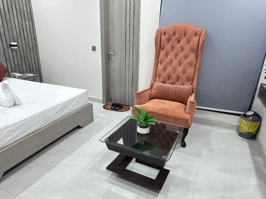 Quarto moderno com cama, poltrona estofada, mesa de centro de vidro e uma planta, e parede cinza.