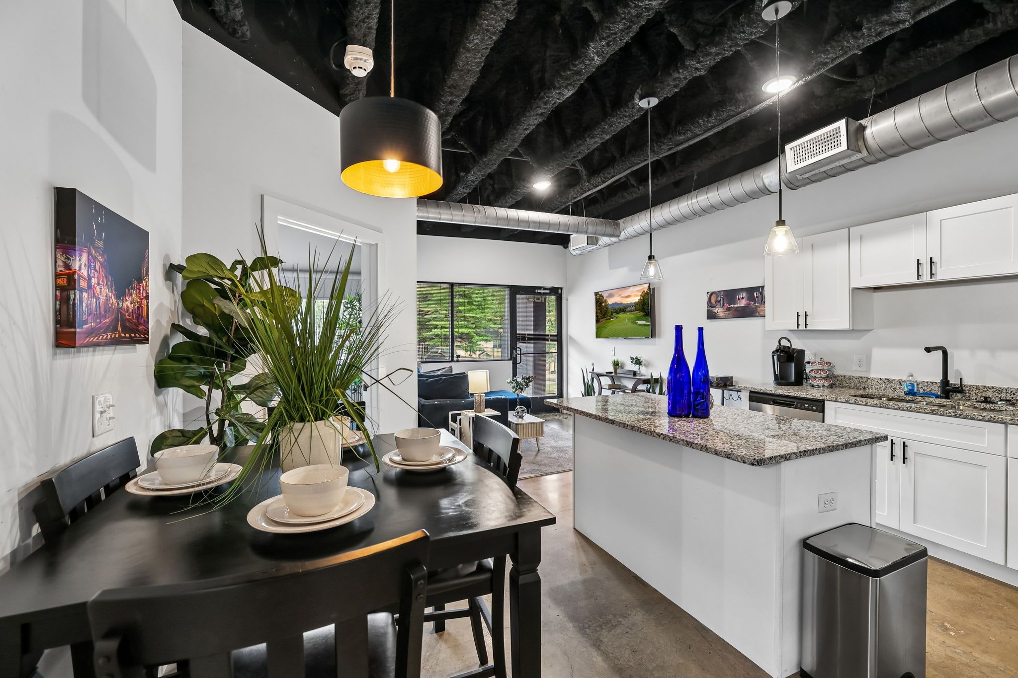 A modern kitchen with white cabinets, a granite countertop, and a dining area with a black table and chairs.