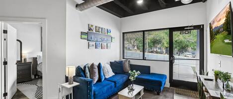 A modern living room with a blue sofa, a coffee table, and a large window with blinds.