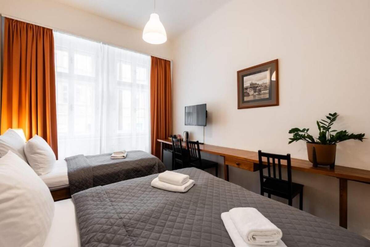 Ein Hotelzimmer mit zwei Betten, einem Schreibtisch, einem Sessel, einem Fernseher und einem gerahmten Bild an der Wand.