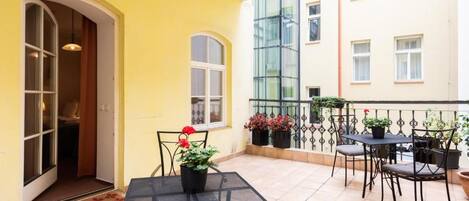 A yellow building with a patio area featuring a table and chairs, potted plants, and a view of adjacent buildings.