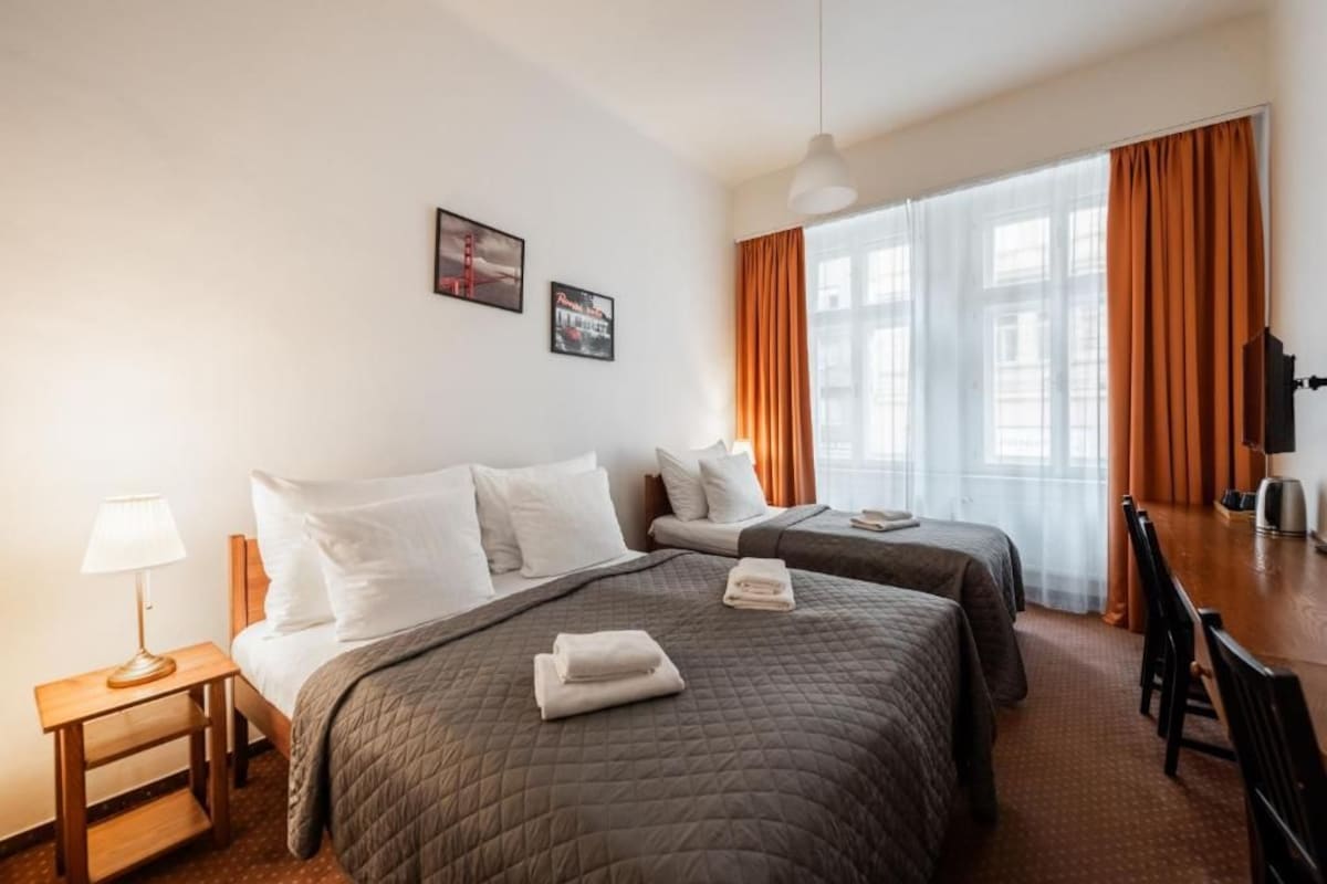 A hotel room with two beds, a desk, a chair, a lamp, and a window with curtains.