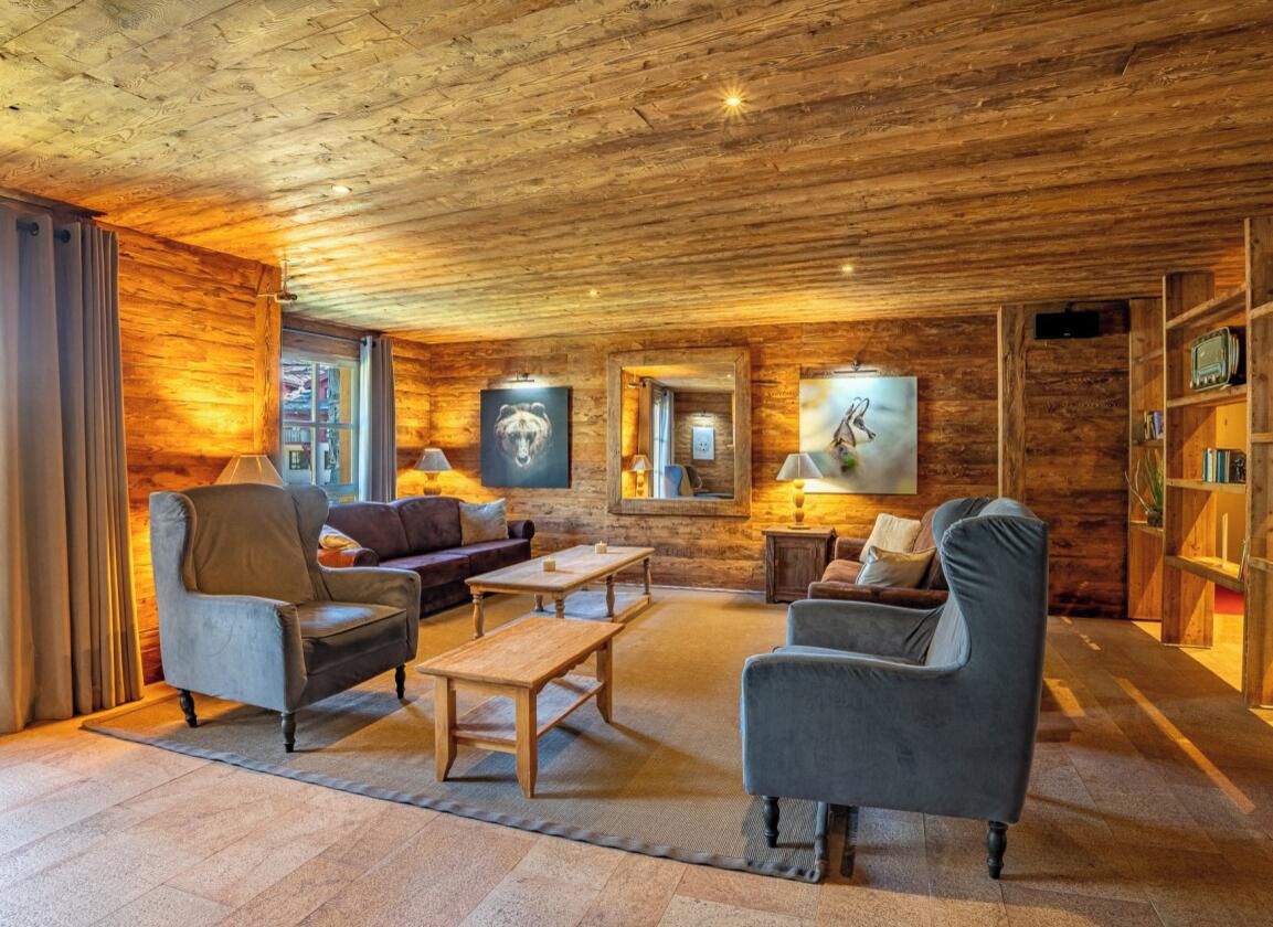 Un salon chaleureux avec des murs et un plafond en bois, un ensemble de canapés, une table basse et une bibliothèque.