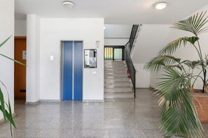Un couloir avec une porte bleue, un escalier et une plante en pot.