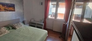 Ein Schlafzimmer mit einem Bett, einem Nachttisch, einem Fenster mit Vorhängen und einer Heizung.