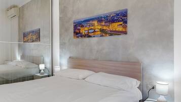 A hotel room with a large bed, a bedside table, a lamp, a mirror, and a cityscape painting on the wall.