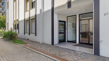 A modern building with a stone-paved entrance, large windows, and a number '97' on the wall.