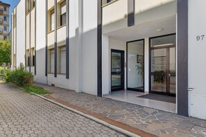 Un bâtiment moderne avec une entrée pavée de pierres, de grandes fenêtres et le chiffre « 97 » peint sur le mur.