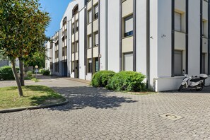 Un edificio moderno con entrada pavimentada, un árbol y una moto estacionada.