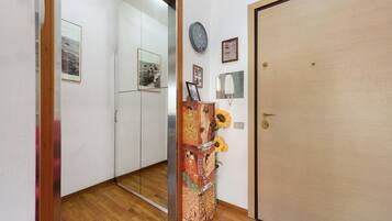 A hallway with a wooden floor, a door with a keyhole, and a wall with a clock and framed pictures.