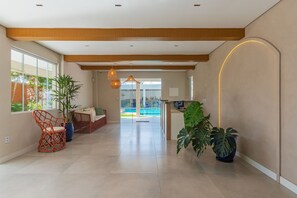 Un espace intérieur spacieux avec vue sur la piscine, agrémenté de meubles en osier et de plantes en pot.