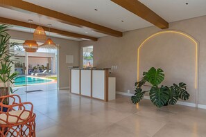 Uma área de recepção moderna com vista para a piscina, um balcão de atendimento e plantas tropicais.
