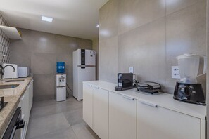 A modern kitchen with a built-in refrigerator, a water dispenser, a coffee maker, and a blender. - Villa Pilar Cumbuco House With Pool by Carpediem (Caucaia)