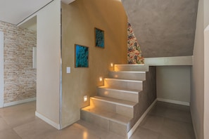 A staircase with a stone wall on one side and a plain wall on the other, with two framed artworks on the plain wall. - Villa Pilar Cumbuco House With Pool by Carpediem (Caucaia)