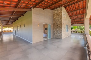 A spacious indoor area with a high ceiling, a stone wall, and a view of greenery outside. - Villa Pilar Cumbuco House With Pool by Carpediem (Caucaia)