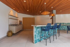 Une cuisine avec un plafond en bois, une cuisinière à gaz et un coin bar avec des chaises bleues.