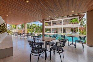 Un espace extérieur abrité, doté de tables et de chaises, d’une piscine et offrant une vue sur un bâtiment à la façade en pierre.