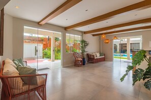 Amplo espaço interno com teto alto, grandes janelas e vista para uma piscina externa.