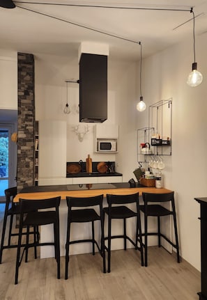 Une cuisine moderne avec un îlot central, des tabourets de bar noirs et des luminaires suspendus.