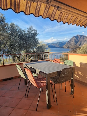 An outdoor patio with a table and chairs, overlooking a mountainous landscape and a body of water. - Vrbo Property (Lombardia)