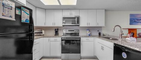 A modern kitchen with white cabinets, a stainless steel refrigerator, a microwave, an oven, and a dishwasher.