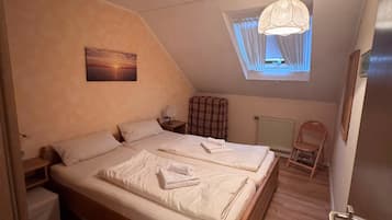 A bedroom with a wooden bed, a nightstand, a chair, a window with curtains, and a painting on the wall.