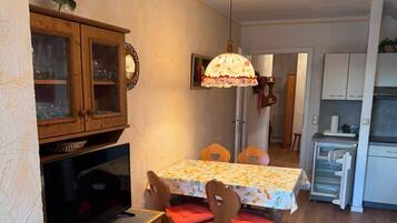 A compact kitchen with a dining area, wooden cabinets, a television, and a refrigerator.