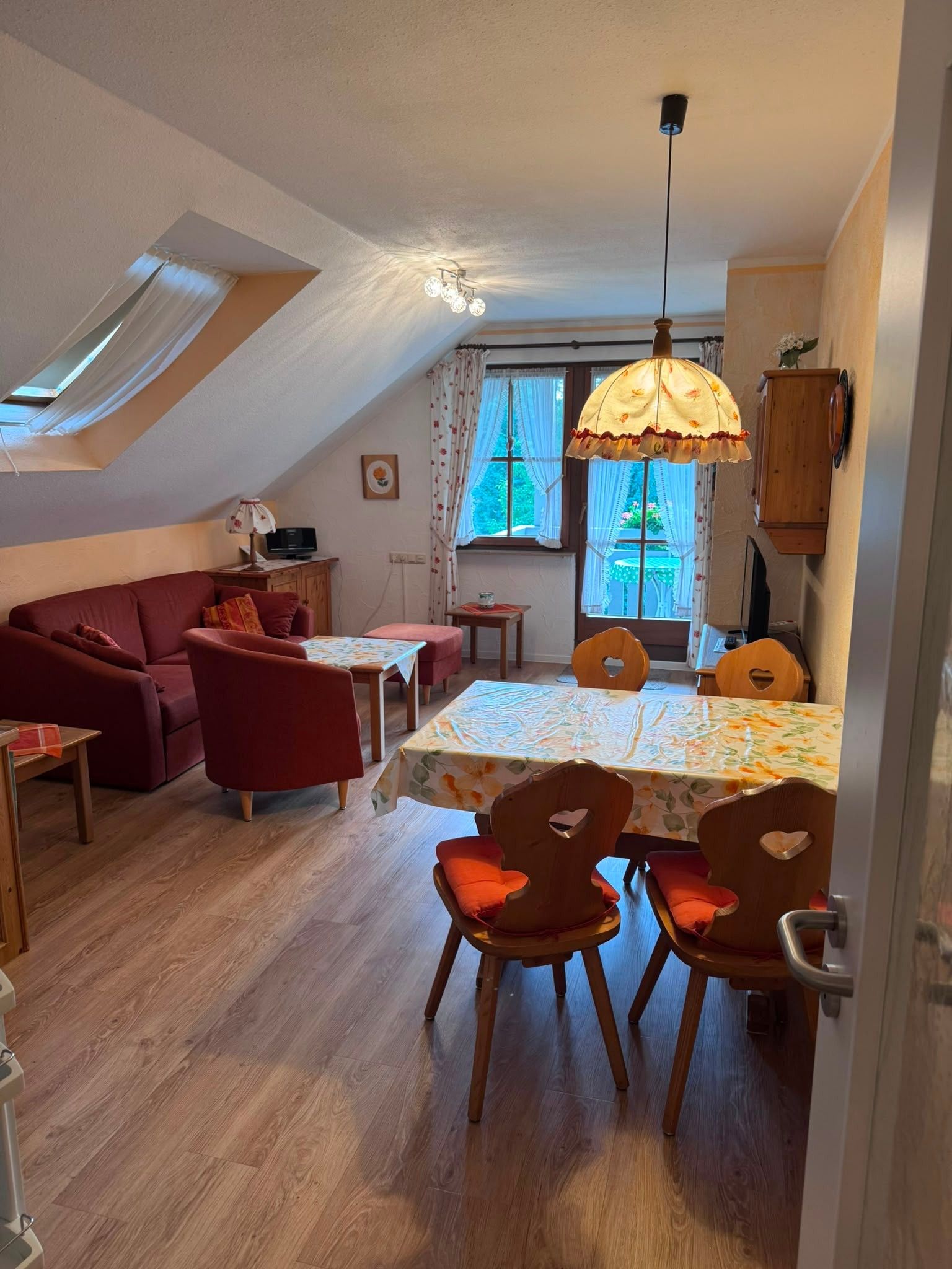 Un salon confortable avec un canapé, une table à manger et des chaises, un luminaire au plafond et une fenêtre avec des rideaux.