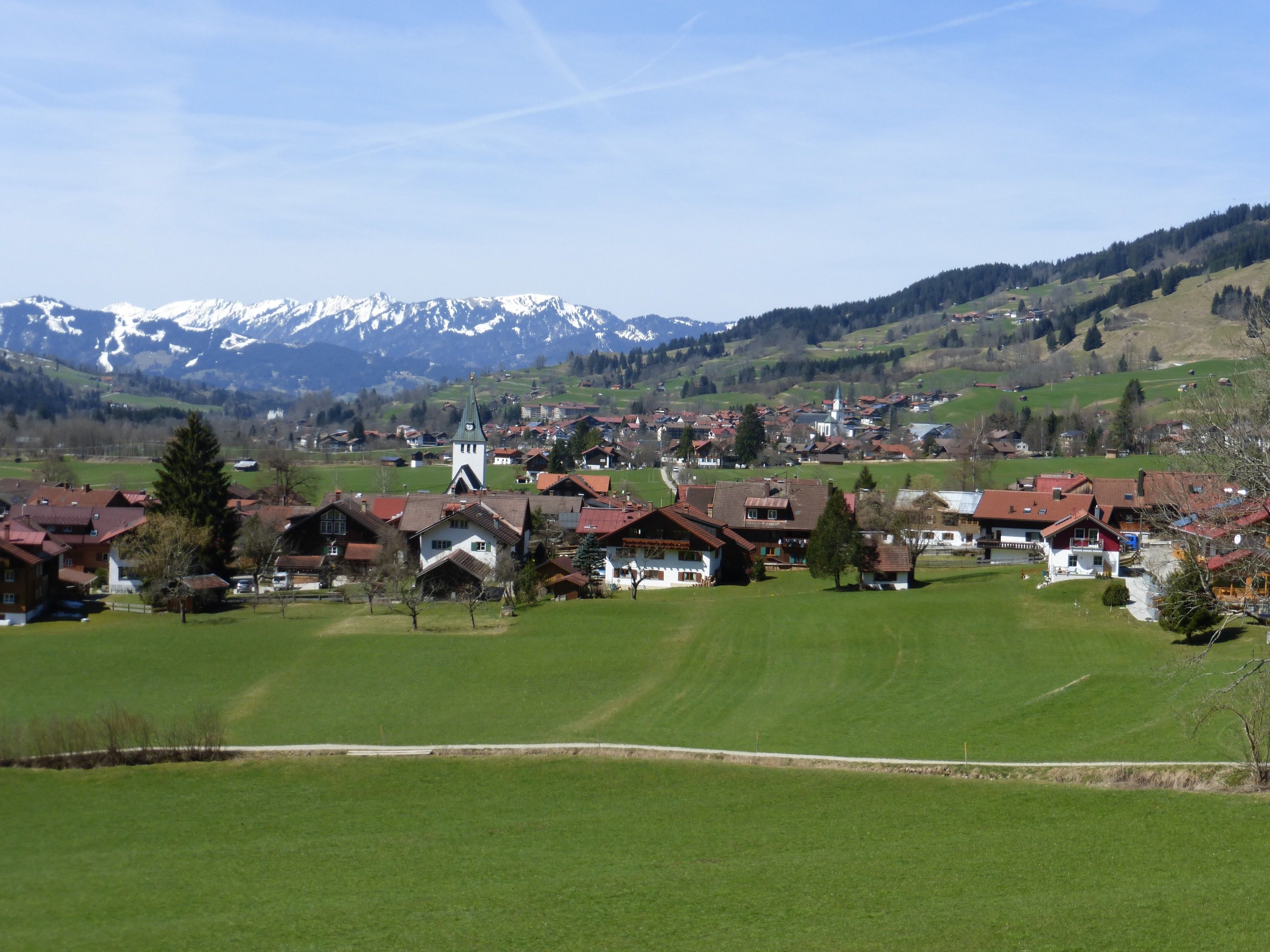 A village with traditional houses, a church, and snow-capped mountains in the background.