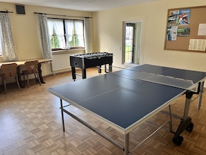 Una habitación con dos mesas de ping pong, una mesa de fútbol de mesa y un tablón de anuncios con fotografías.