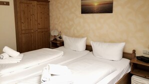 Una camera d'albergo con due letti, un armadio in legno, un quadro appeso al muro raffigurante un tramonto e un comodino con una lampada.