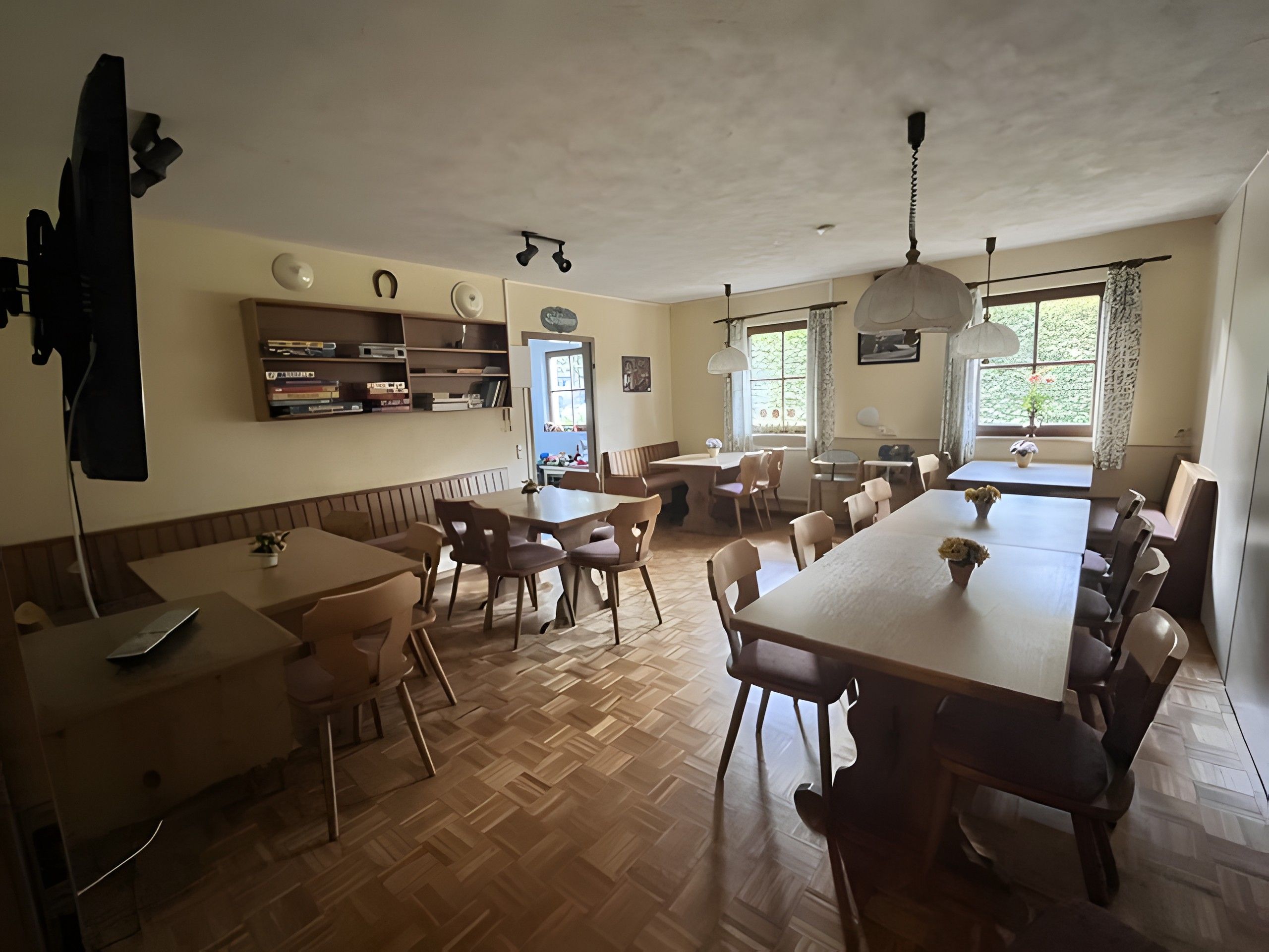 A dining area with multiple tables and chairs, a ceiling fan, and a window with curtains.