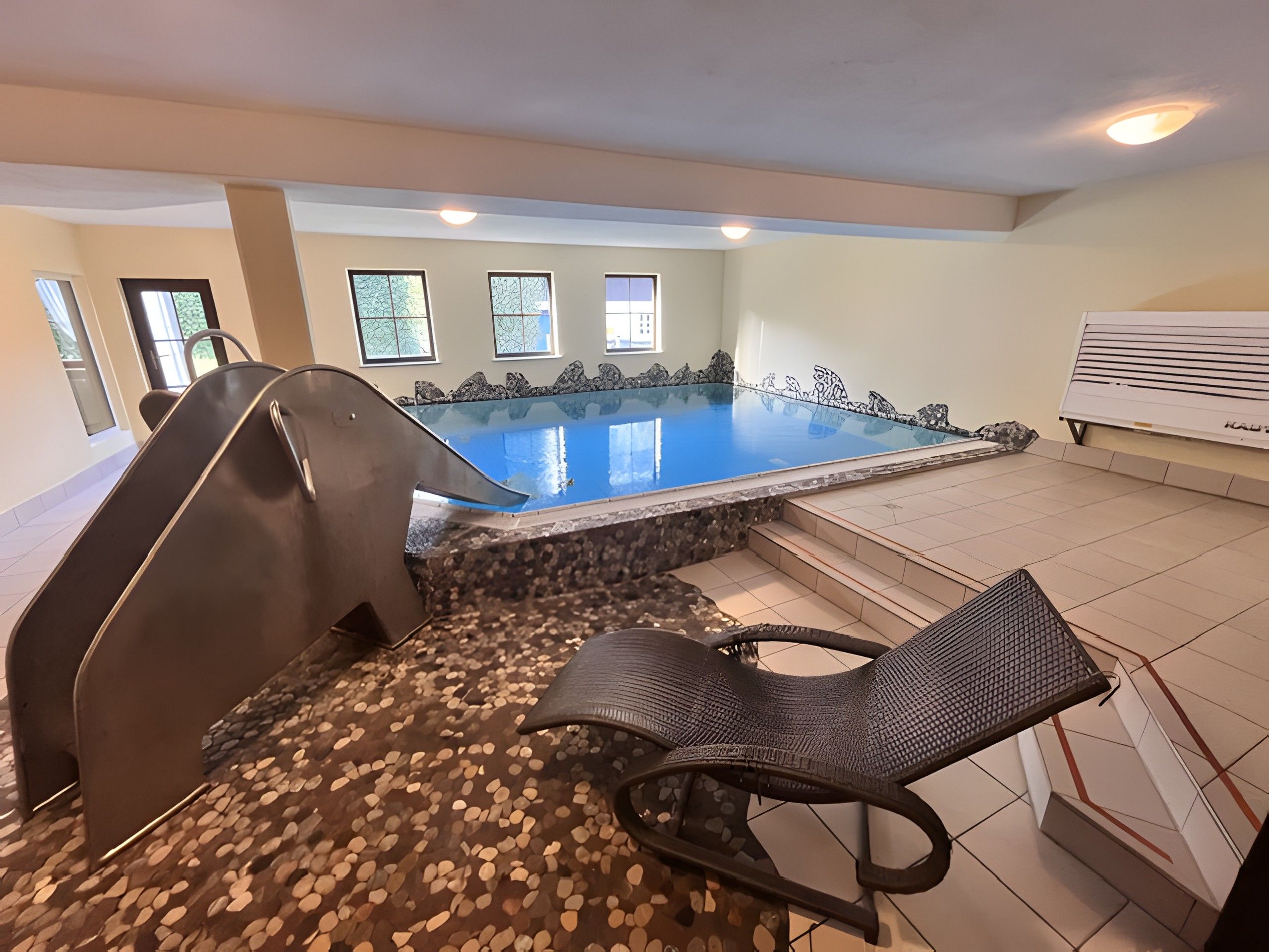 Ein Hallenbad mit Steinrand, einer Rutsche und einer Liege.