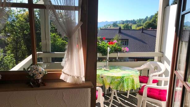 Un balcone con tavolo e sedie, vista su una casa con tetto in tegole e vegetazione sullo sfondo.