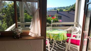 Ein Balkon mit Tisch und Stühlen, Blick auf ein Haus mit Ziegeldach und grüne Bepflanzung im Hintergrund.