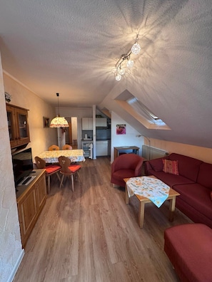 Un espacio habitable compacto con comedor, un sofá rojo, una mesita y una cocina al fondo.