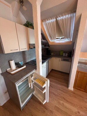 Cocina compacta con piso de madera, horno integrado y ventana con cortinas.