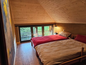 Une chambre avec deux lits, un plafond en bois et un balcon doté d’une balustrade.