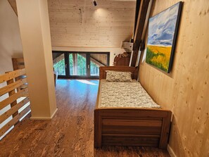 Une chambre à coucher avec un lit en bois, un tableau accroché au mur et une vue sur l’extérieur grâce à de grandes fenêtres.